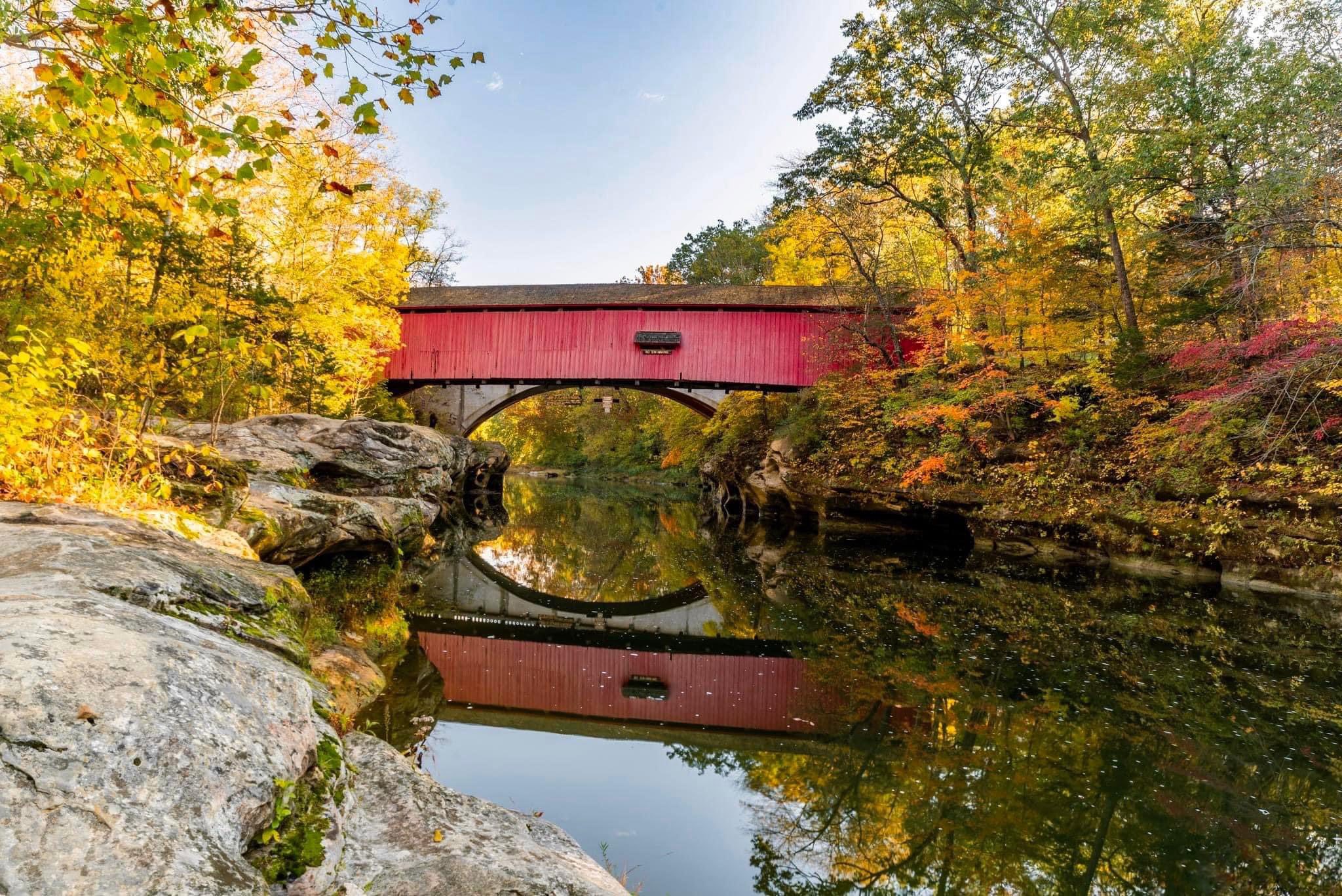 Covered bridge reflected in the creek in autumn
